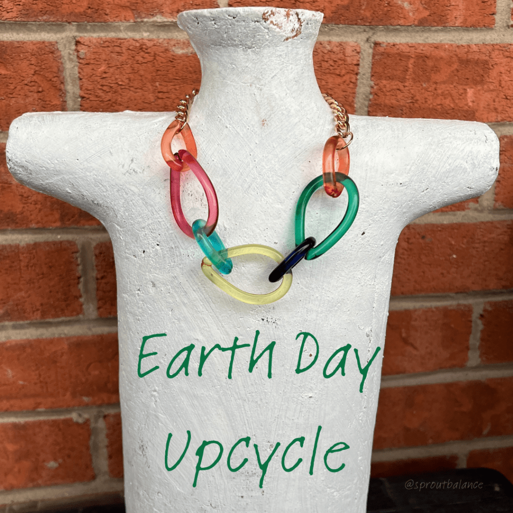 Colourful Teardrop Necklace with very short gold chain. It is hanging on a white ceramic bust in front of a brick wall. 